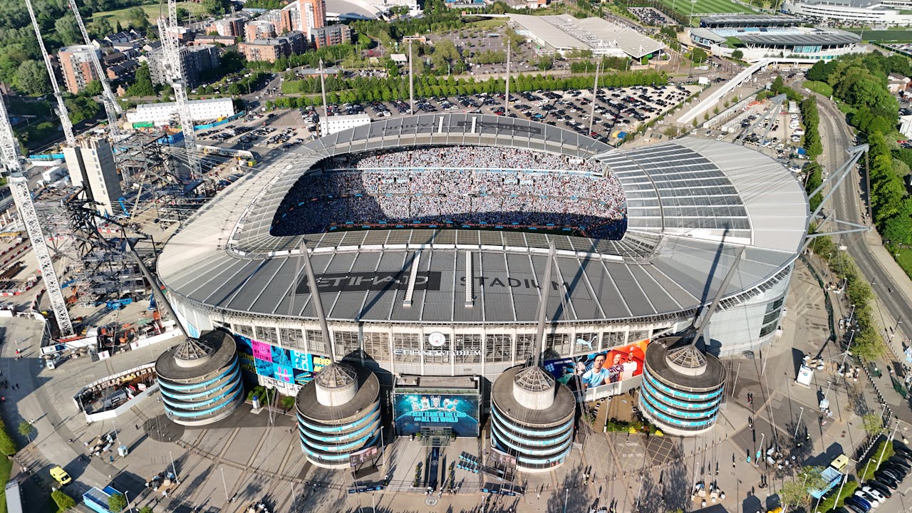 Home Drone shot of a packed Etihad Stadium in Manchester, England, showcasing a vibrant cityscape.