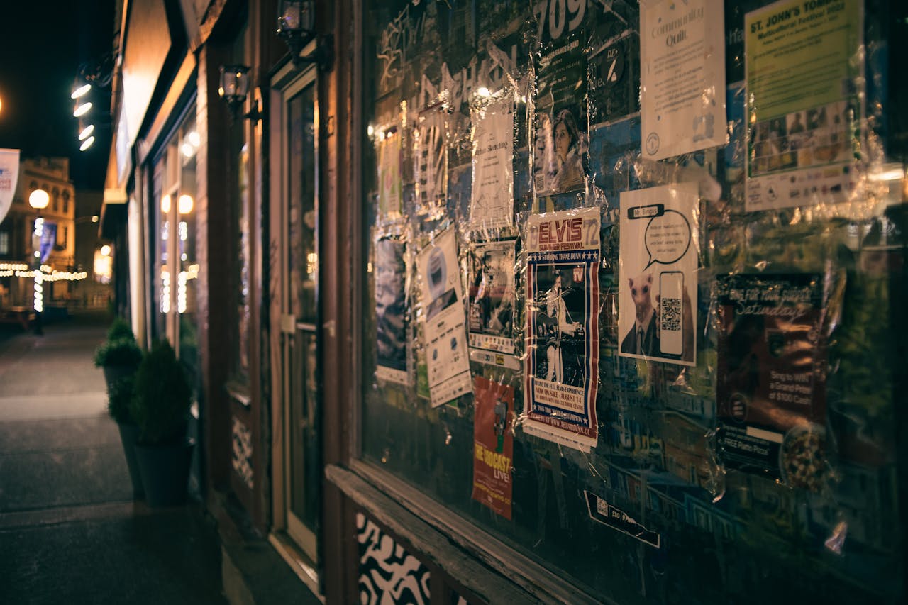 Close-up of a store front displaying various posters illuminated by ambient streetlights at night.